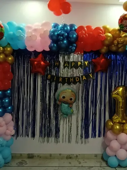 A Cocomelon themed birthday decoration for a home setting. This setup uses a blue shimmer curtain backdrop, a balloon frame in multiple colors, a 'Happy Birthday' banner, and Cocomelon character balloons.