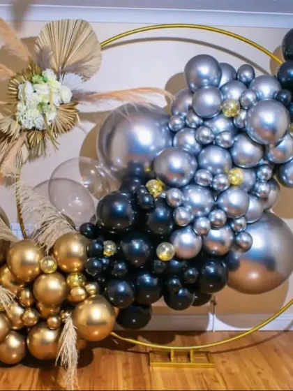 A modern and chic circular ring backdrop decorated with a black, gold, and silver balloon garland and pampas grass.
