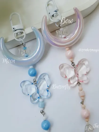 Our moonlight whimsy charms in dreamy blue and blush pink. Each one features a large crescent moon, a translucent butterfly, and coordinating beads, perfect for adding a touch of magic to your bag.