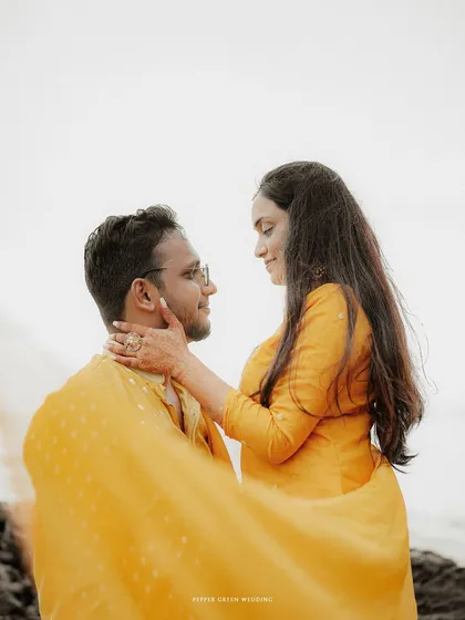 A tender moment from a beach pre-wedding shoot, the warm yellow of their outfits contrasting beautifully with the soft light.