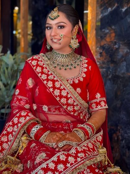 A smiling portrait of a bride ready for her wedding. The look features a flawless base, a simple maang tikka, and jewelry with green accents.