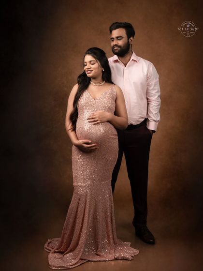 A classic and elegant studio portrait of a couple. The mom-to-be shines in a rose-gold sequin mermaid gown against a timeless painterly backdrop.