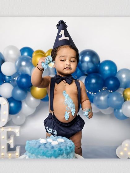 A baby boy stands proudly next to his first birthday cake, a little bit of frosting already on his hand and face. This shot captures the beginning of a fun and messy celebration.