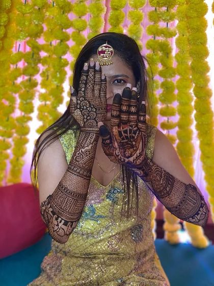 A happy bride peeking through her beautifully decorated hands at her mehandi ceremony.