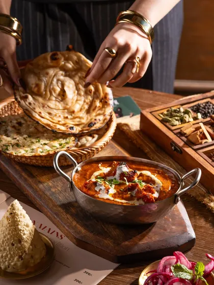 A classic Indian meal of butter chicken and naan. The hand tearing the naan adds a human touch and makes you want to dig in.