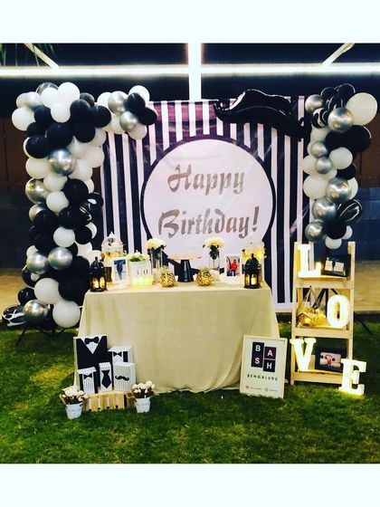 A chic black, white, and silver birthday setup for an outdoor evening party. We created a stylish photo backdrop with a striped panel, a custom 'Happy Birthday' sign, and two beautiful balloon columns.
