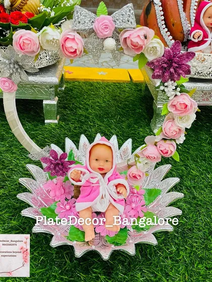 For a baby shower, I created this custom platter featuring a baby doll in a pink robe, nestled in a decorative floral cradle. This is an example of the themed and personalized decorations I offer for seemantham ceremonies.