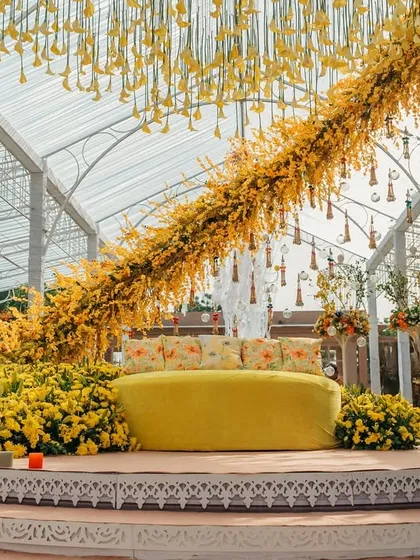 Another view of the 'Sunshine' Haldi ceremony stage. A massive diagonal garland of yellow flowers stretches across the glass ceiling, creating a dramatic and joyful focal point.
