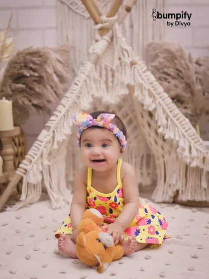 A close up of this little sunshine in our boho teepee setup, holding her teddy bear. The colorful details of her dress pop against the neutral background.