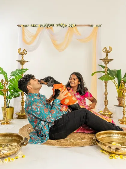 A brother and sister have fun with their dachshund during a Diwali photoshoot. The dog gives a happy lick, adding a touch of playful chaos to the festive scene.