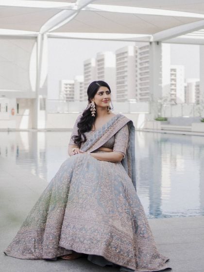 A full-length portrait of the bride seated by a pool. Her elegant lehenga and the modern, bright setting create a sophisticated and chic image.