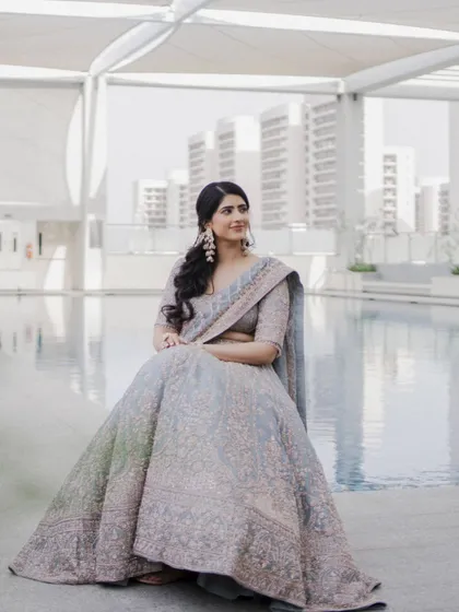 The bride is seated by the pool, her elaborate grey lehenga spread out, creating a stunning portrait against the modern cityscape.