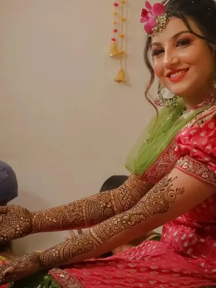 A happy bride smiling and showing off her elegant full-arm mehndi, which complements her pink and green outfit perfectly.