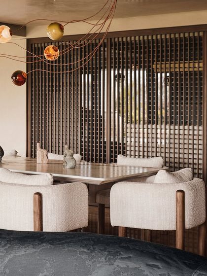 A detail of the dining area, focusing on the textured chairs and the wooden screen. The play of light through the screen adds depth and pattern to this serene dining space.