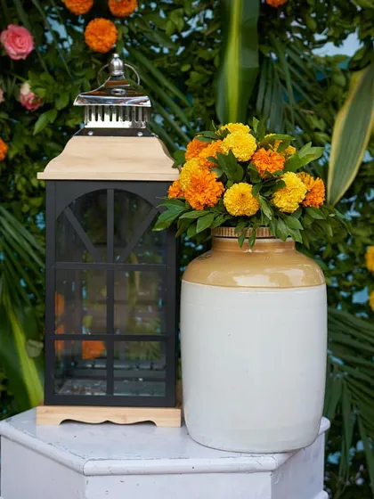 A simple yet elegant decor detail. A classic lantern paired with a vase of fresh marigolds against a lush green backdrop adds a touch of rustic charm.