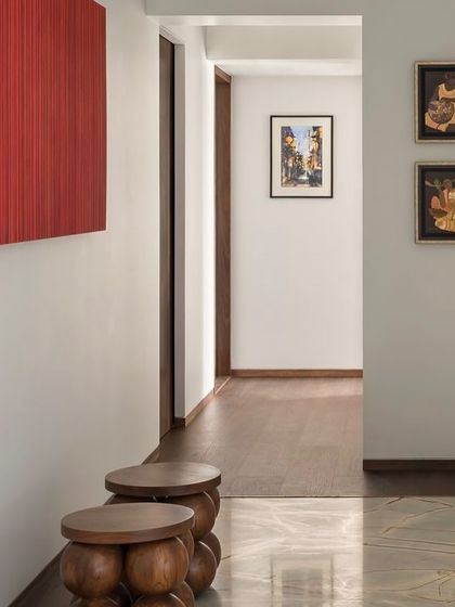 A closer look at the art and details in the West Coast Residence hallway. The wooden stools and the vibrant red artwork create a strong visual statement against the clean white walls.