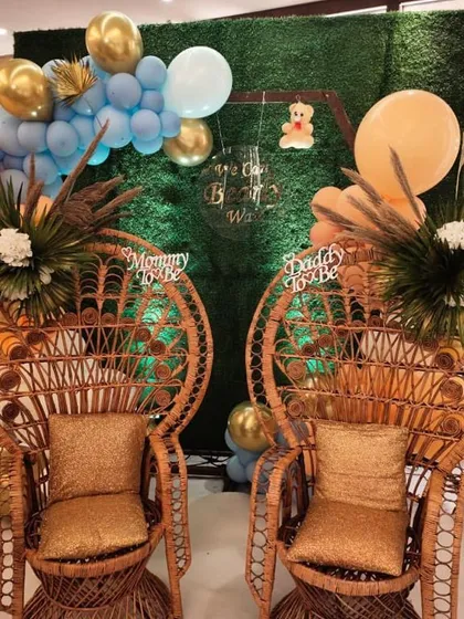We make sure the parents-to-be feel special with dedicated seating. Here, we used ornate peacock chairs labeled "Mommy to be" and "Daddy to be" against a lush greenery wall backdrop for a stylish, boho-chic baby shower.