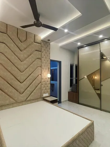 This bedroom design combines a floor-to-ceiling wardrobe with tinted mirror and glass shutters. The headboard extends to the ceiling with gold strip inlays, giving the room an elite and spacious feel.