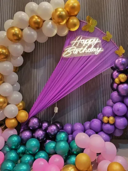 A detailed shot of the purple, white, and gold birthday decoration, highlighting the butterfly accents and the glowing neon sign.