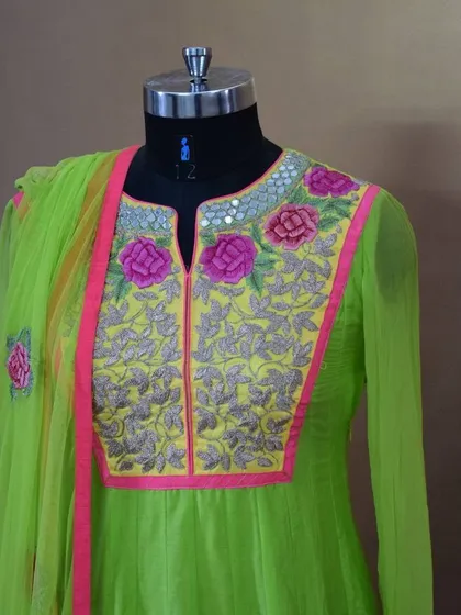 The neckline of our lime green Anarkali features a combination of thread embroidery and mirror work. The vibrant pink piping makes the detailed craftsmanship pop.