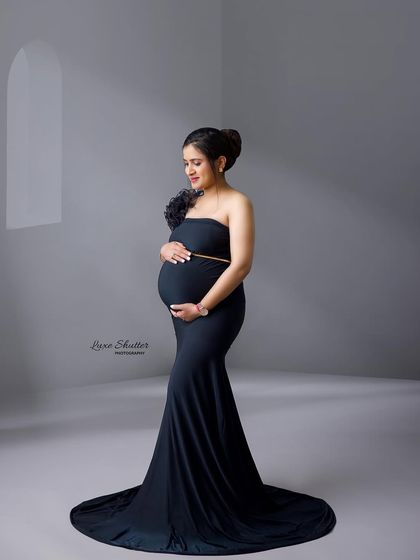 A simple and elegant black gown, accented with a floral detail on the shoulder. The soft window lighting adds a gentle, artistic touch.