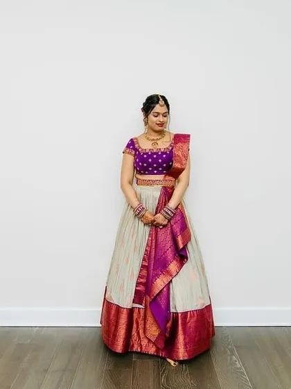 The bride stands gracefully in her ivory and purple lehenga, a picture of timeless elegance.