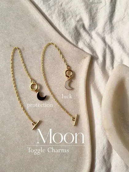 A closer look at the moon toggle charms. Each birthstone holds a special meaning, and wearing one can help with luck and manifestation. Here you see black onyx for protection and white moonstone for luck.