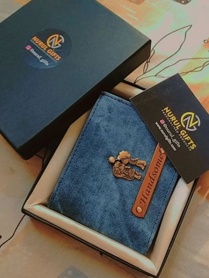 A handsome blue denim wallet with a 'couple' charm, shown with its branded box and business card.