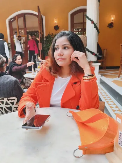 A candid-style shot sitting at a cafe table in my orange coat, showing how the outfit works in a casual, seated setting.