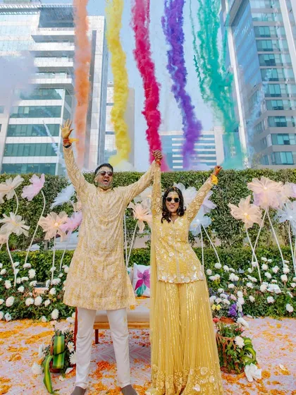 A full-shot of the couple's Haldi celebration, with a rainbow of smoke creating a spectacular backdrop for their joyous moment.