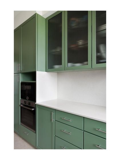 Custom kitchen cabinetry painted in a soft green. The design includes a mix of solid and fluted glass doors, providing both concealed and visible storage for crockery and appliances.