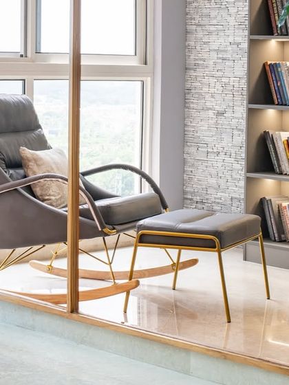 A detail shot of the contemporary rocking chair with its elegant golden frame, set against the backdrop of the city view. Comfort and sophistication combined.