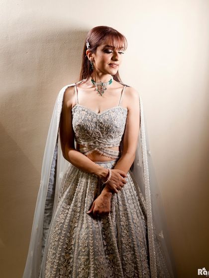 An elegant full-length portrait of the bride-to-be. The soft, diffused light and simple background allow her beautiful caped lehenga and confident posture to take center stage.