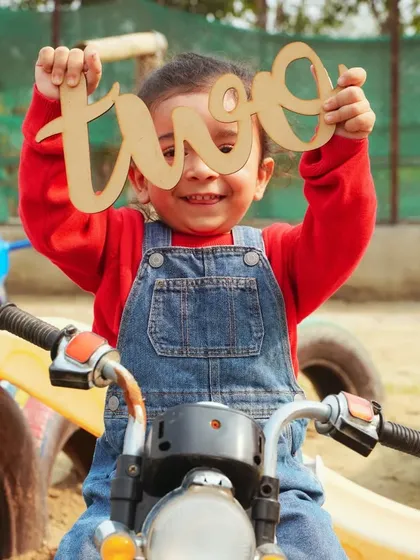 Celebrating turning two with an outdoor photoshoot. This little one is having a blast on a toy motorcycle in a playful park setting.