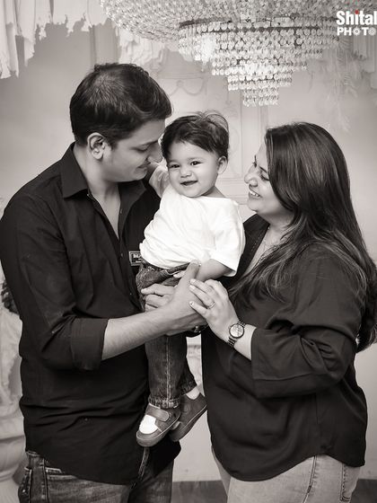 A classic black and white family portrait. The image captures the loving gazes between the parents and their happy child, creating a timeless memory.