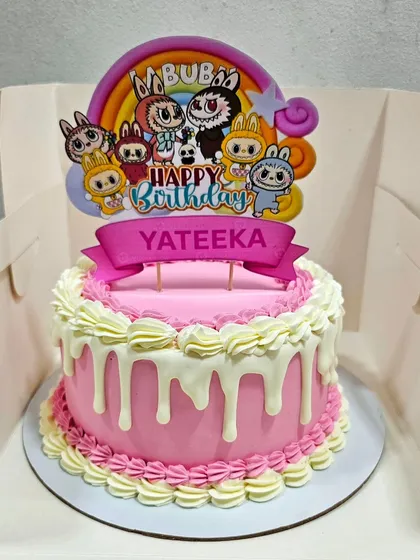 A modern buttercream cake with a pink base, white chocolate drip, and classic piped borders, topped with a cute Labubu character.