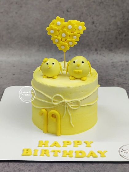 A cute yellow chick cake, perfect for a baby shower or a young child's birthday. The two chicks and heart made of flowers make for a very sweet design.