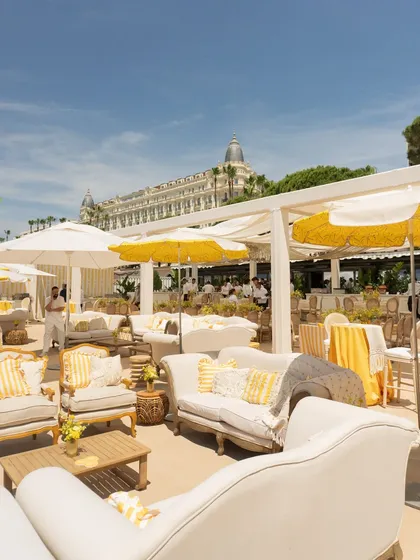 A wide view of the Mehendi lounge setup in Cannes, with white sofas, yellow-striped cushions, and umbrellas, all overlooking the beautiful beach.