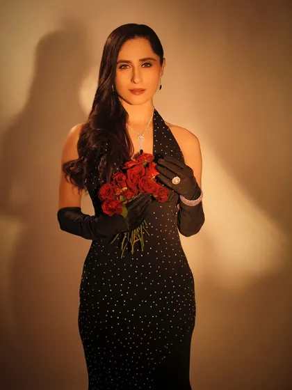 A beautiful medium shot that focuses on the contrast between the dark outfit and the bright red roses. The makeup is kept classic and elegant to match the overall theme.
