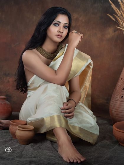 A seated portrait in a traditional white and gold saree, surrounded by rustic props. This setup creates a narrative feel, blending fashion photography with a touch of cultural storytelling.