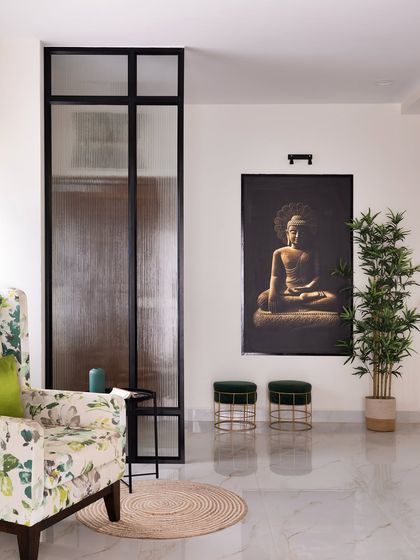 Here, I created a tranquil corner in a living room using a modern glass and metal partition to subtly separate the space. A serene Buddha artwork serves as the focal point, complemented by lush greenery and comfortable seating.