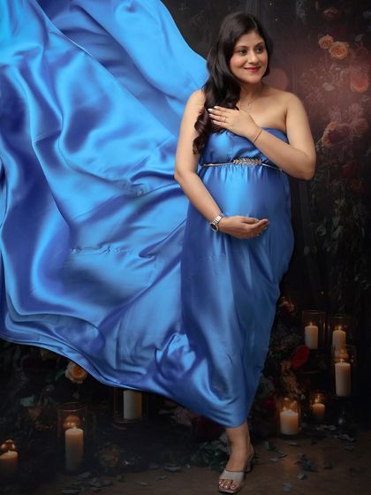 The magic of motherhood, frozen in time. A beautiful blue satin gown flows around the mom-to-be, who is surrounded by the soft light of candles.