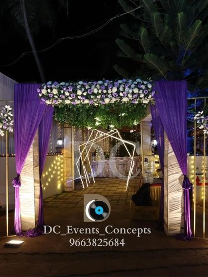 A stunning entrance designed for a Roce ceremony. The purple draping, white floral arrangements, and warm lighting create a welcoming and elegant gateway for the event.