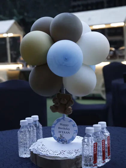 A simple yet sweet table centerpiece with a cluster of matte balloons in muted tones. A small teddy bear and a personalized "Happy Birthday Avyaan" tag complete the look.