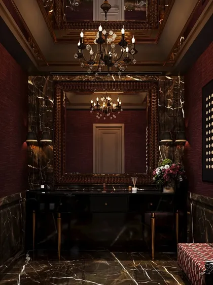 This dramatic powder room concept is wrapped in dark, veined marble and deep red textured walls. An ornate mirror and chandelier add to the opulent, moody atmosphere, creating an unforgettable experience.