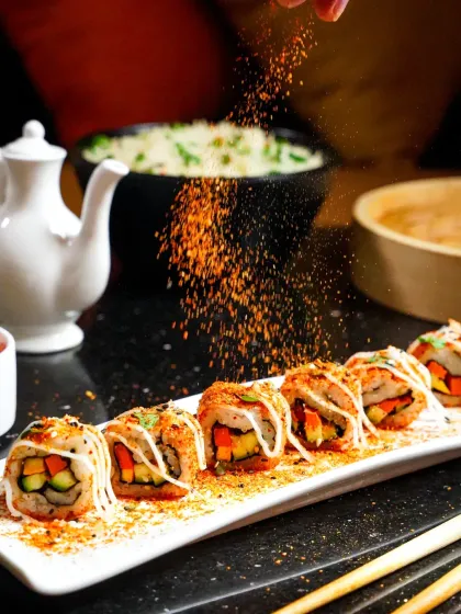 A dramatic action shot capturing a sprinkle of togarashi spice falling onto a platter of beautifully arranged sushi rolls. This close-up focuses on movement and texture, adding a dynamic and appetizing quality to the food photography.