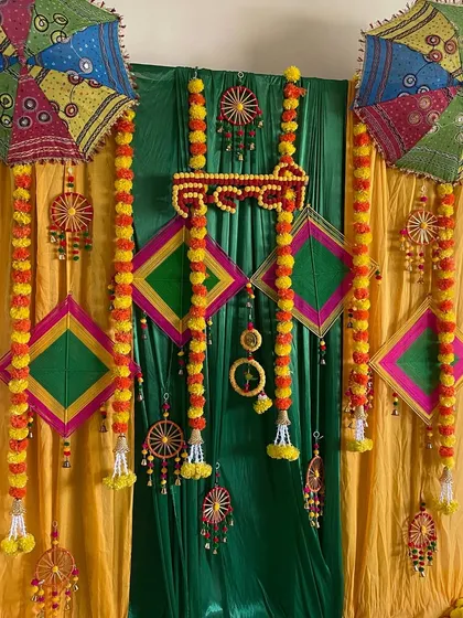 A vibrant Haldi or Mehendi backdrop using colorful drapes, marigold garlands, kites, and traditional Rajasthani umbrellas.