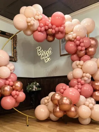 A beautiful "Bride to Be" balloon arch. The organic arrangement of blush, pink, and rose gold chrome balloons on a golden ring frame is perfect for a chic bridal shower.