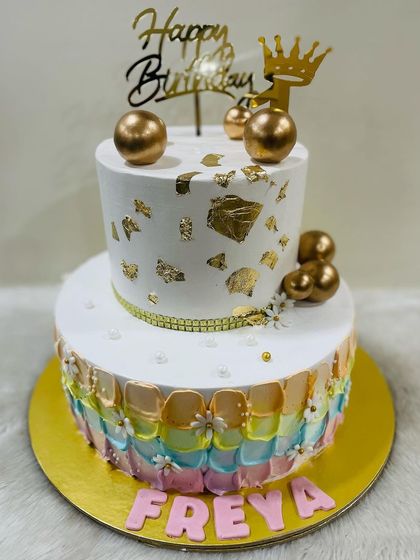 A beautiful two-tiered cake with a pastel rainbow petal effect on the bottom tier and a clean white and gold design on top. A truly sweet slice of paradise.