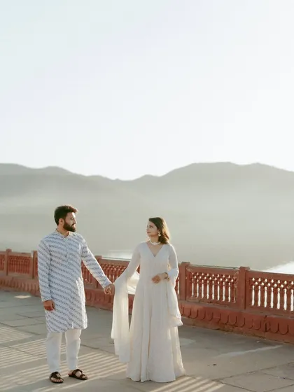 A wide shot capturing the couple holding hands against the hazy mountains and serene waters of Jal Mahal, conveying a sense of peaceful togetherness.